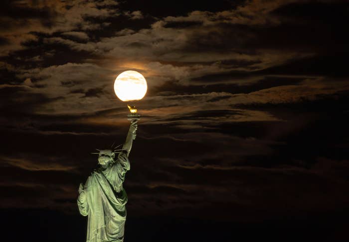 Statue of Liberty at night with a full moon positioned above the torch, creating an illusion of the statue holding the moon
