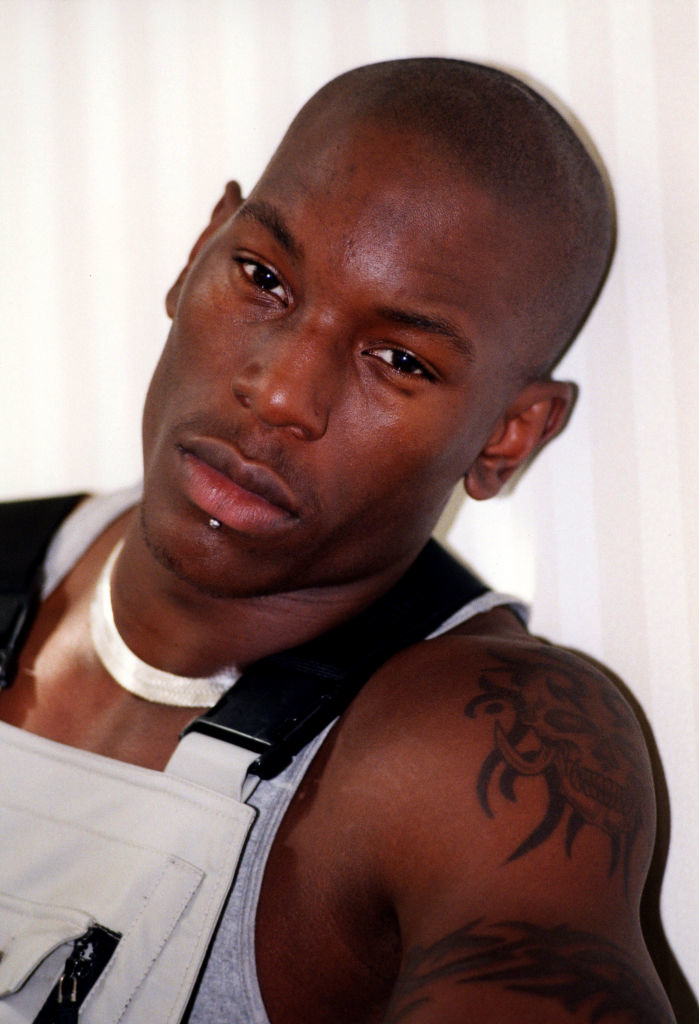 Tyrese Gibson poses in a sleeveless top, showcasing his tattoo and a lip piercing