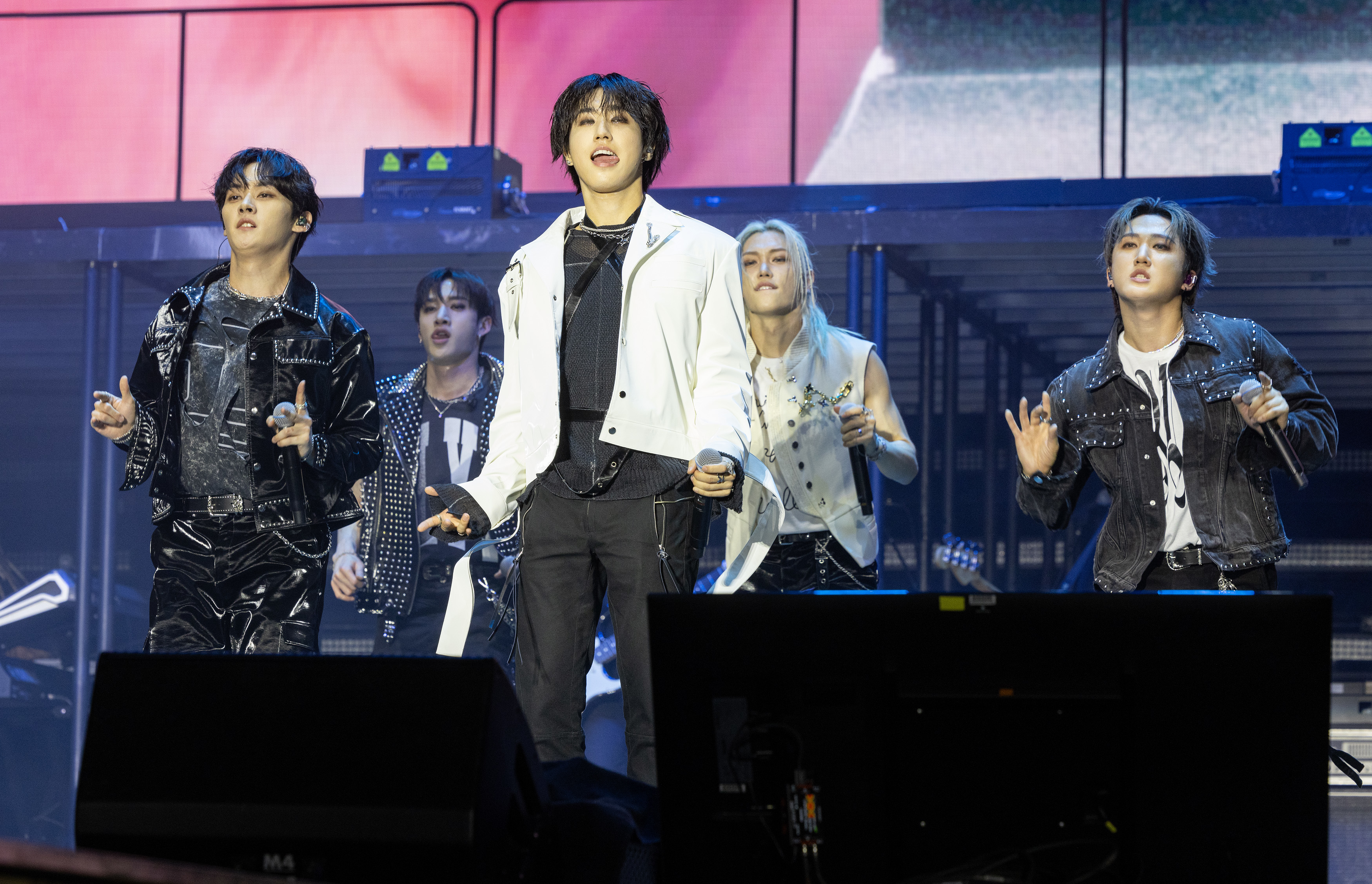 The image shows members of the music group Stray Kids performing on stage. They are wearing stylish outfits while singing and dancing