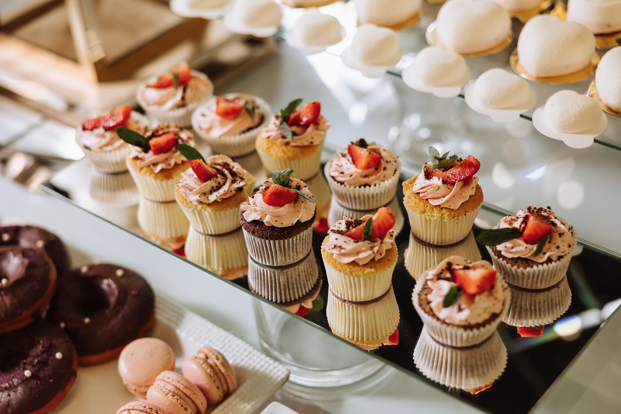 An arrangement of assorted cupcakes topped with fresh strawberries, macarons, and pastries displayed on a mirror tray