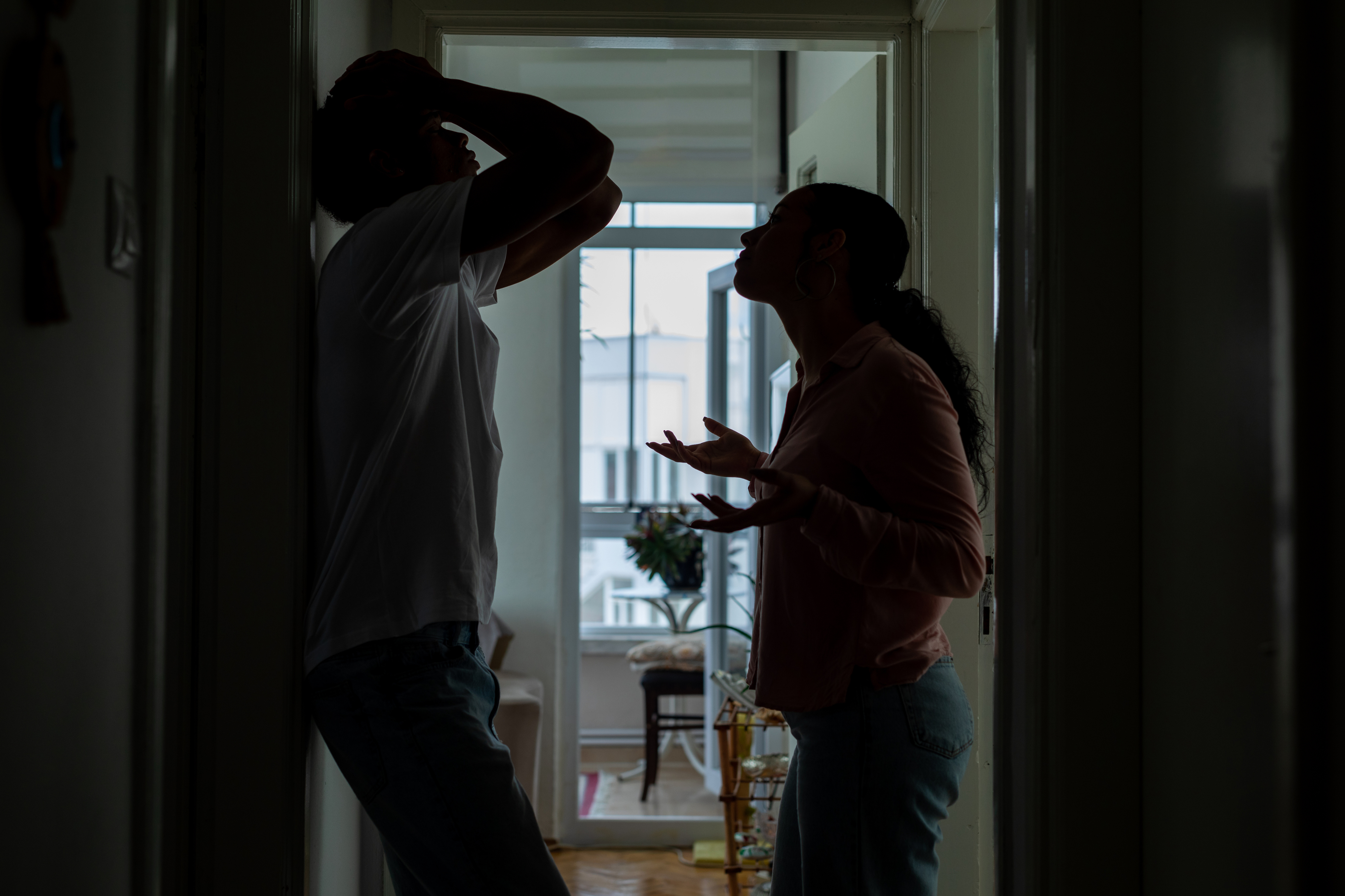 A man and woman are arguing in a corridor, silhouetted against the light from a window in the background