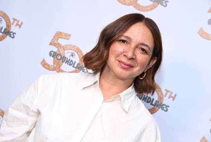 Maya Rudolph at The Groundlings' 50th Anniversary event, wearing a white shirt and hoop earrings, smiling at the camera