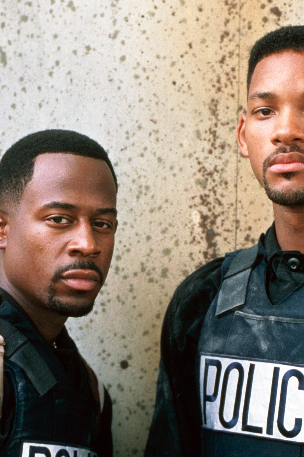 Martin Lawrence and Will Smith dressed as police officers in tactical gear, posing together against a wall
