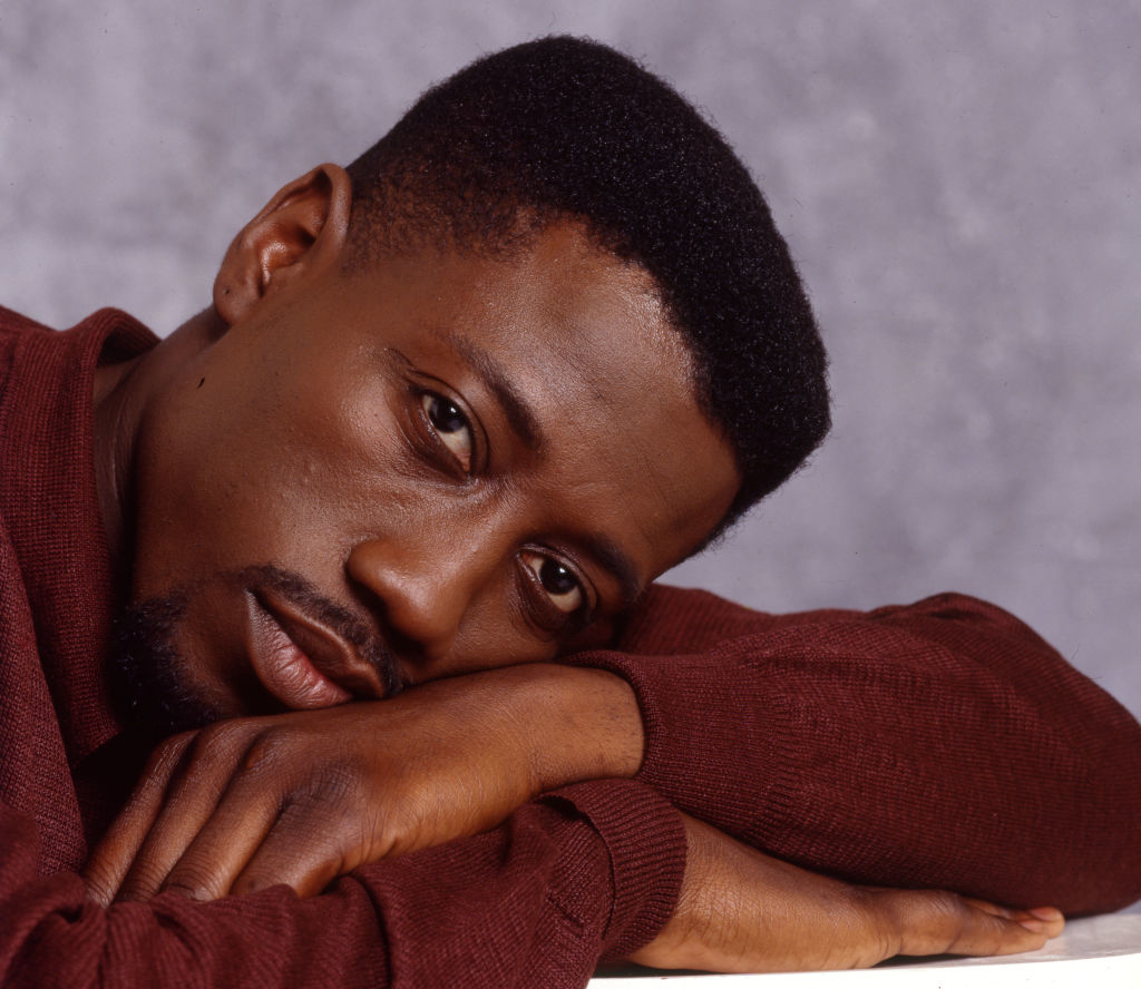 Wesley Snipes is leaning his head on his arm, gazing towards the camera in a contemplative pose
