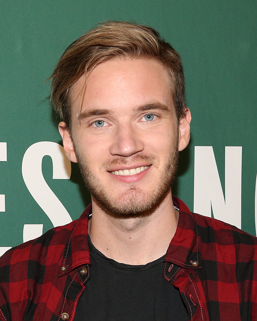 PewDiePie, wearing a black shirt and red checkered jacket, smiles at an event