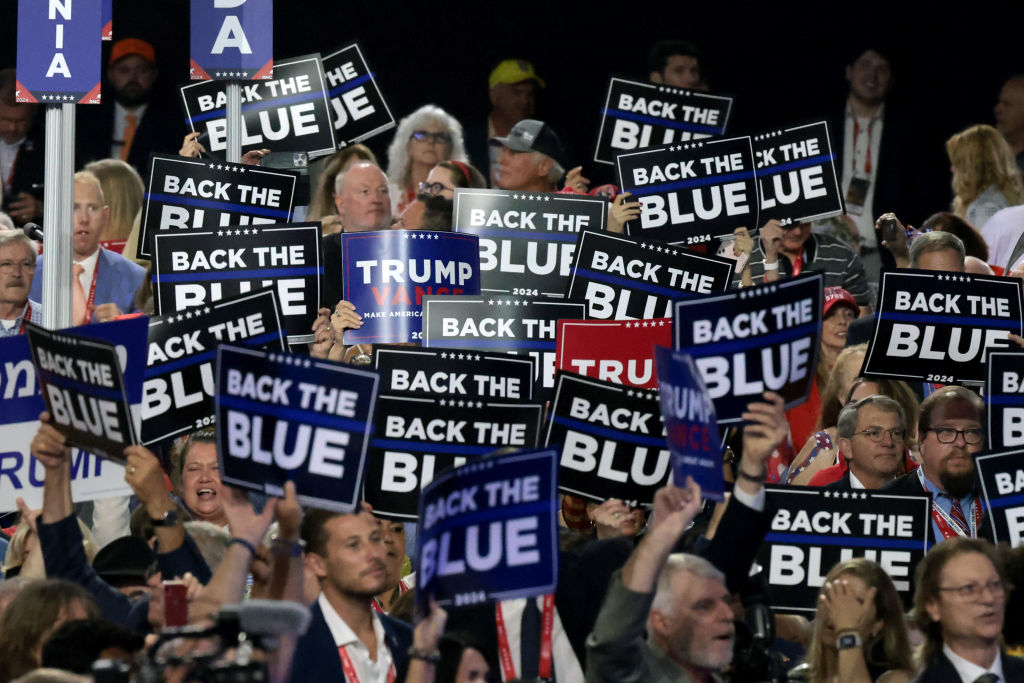 A crowd of people holds &quot;Back the Blue&quot; signs and a &quot;Trump 2024&quot; sign at a rally