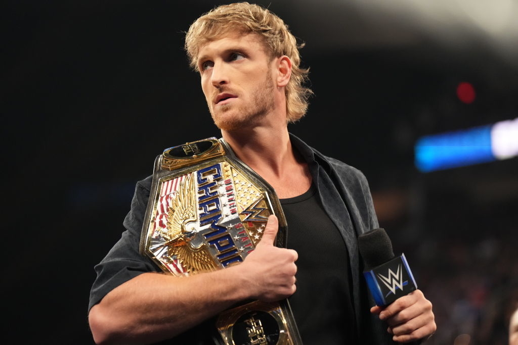 Logan Paul holds a WWE championship belt over his shoulder while holding a microphone during a wrestling event