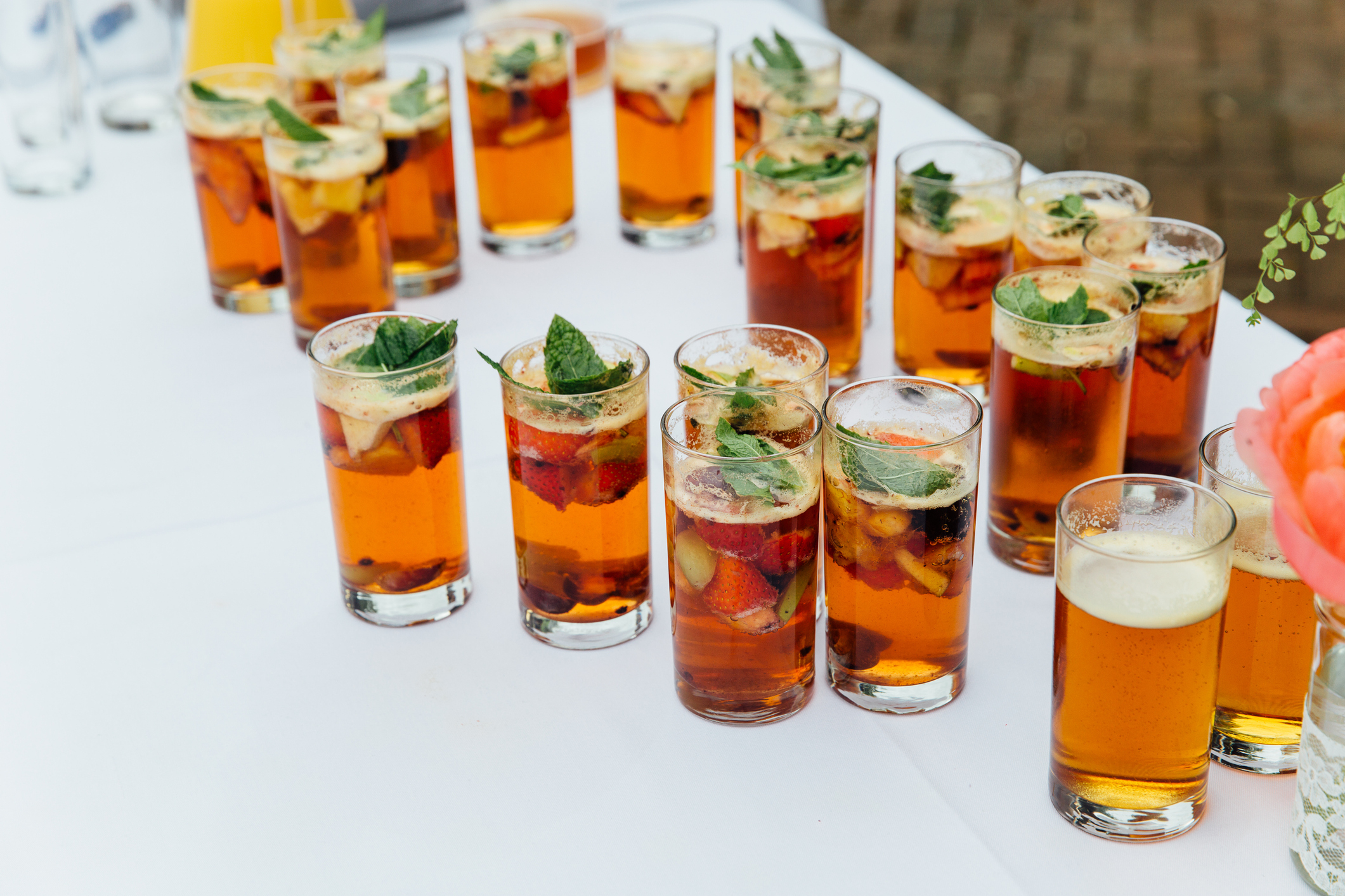 A table filled with multiple glasses of a clear beverage garnished with fruit and mint leaves, likely specialty cocktails or iced tea, set up for an event