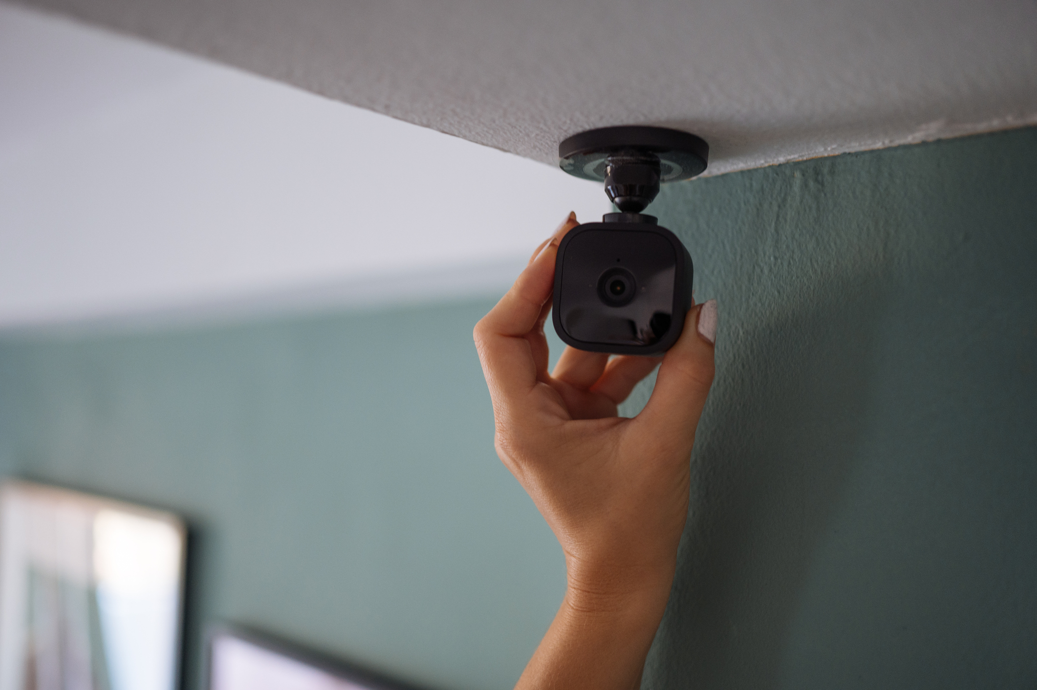 A hand is adjusting a small security camera mounted on a ceiling