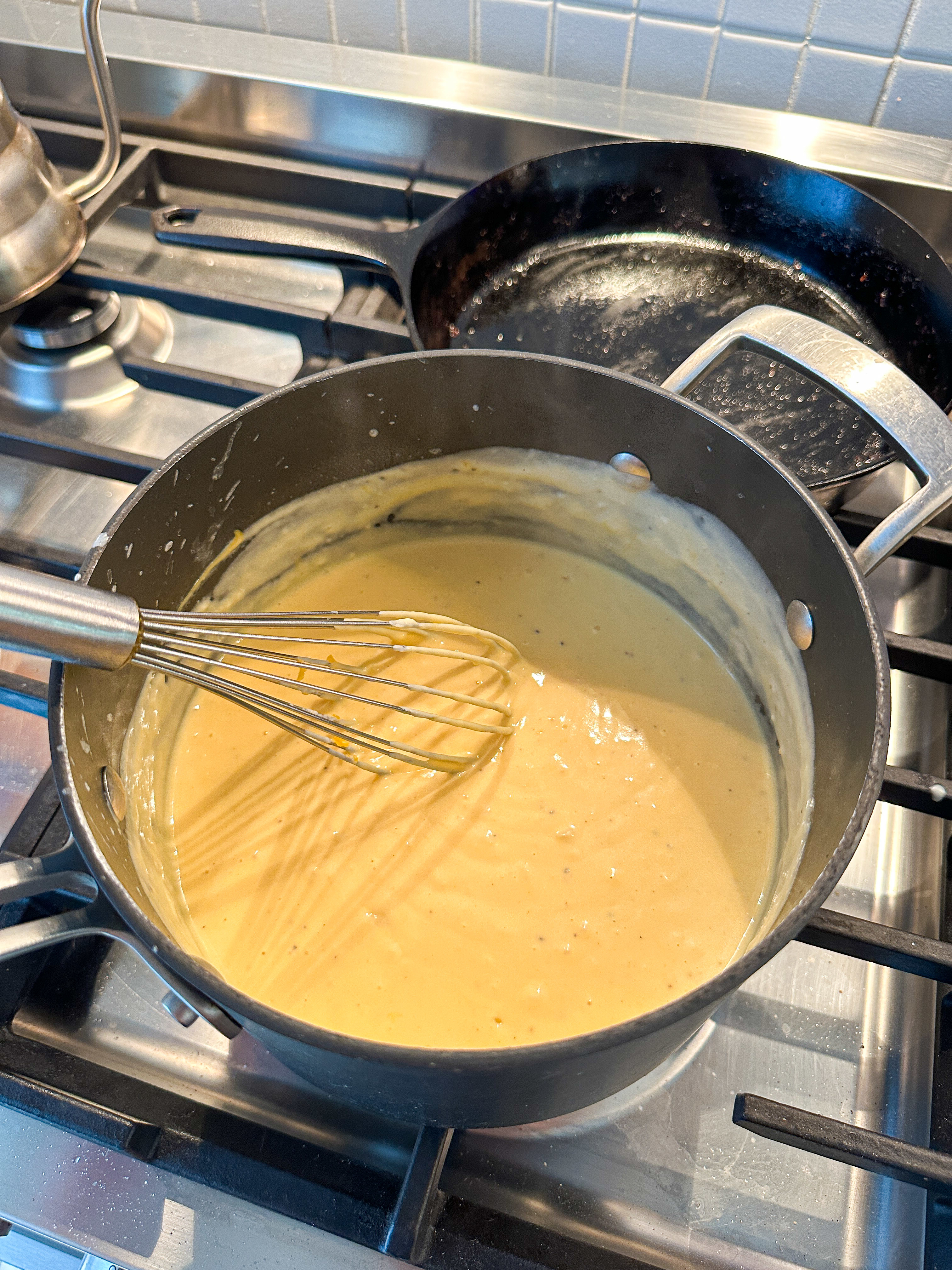 A whisk stirring a creamy sauce in a pot on a stovetop
