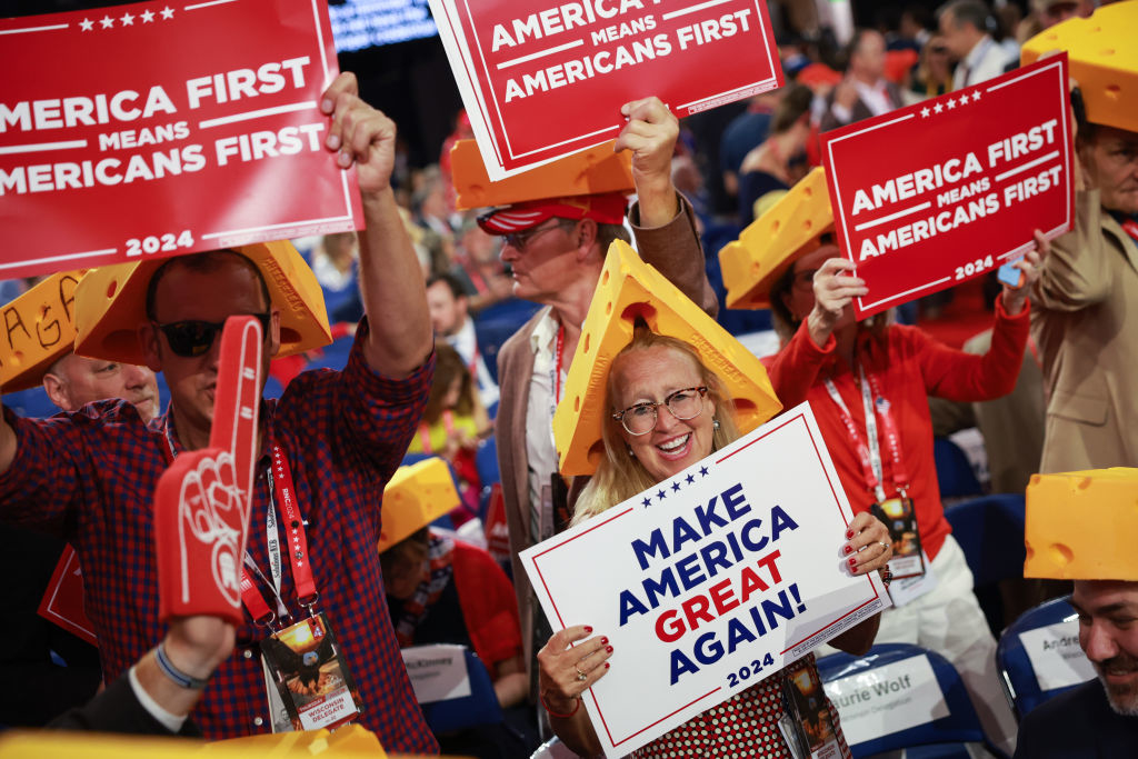 Supporters at a rally wearing cheesehead hats hold &quot;Make America Great Again!&quot; and &quot;America First&quot; signs
