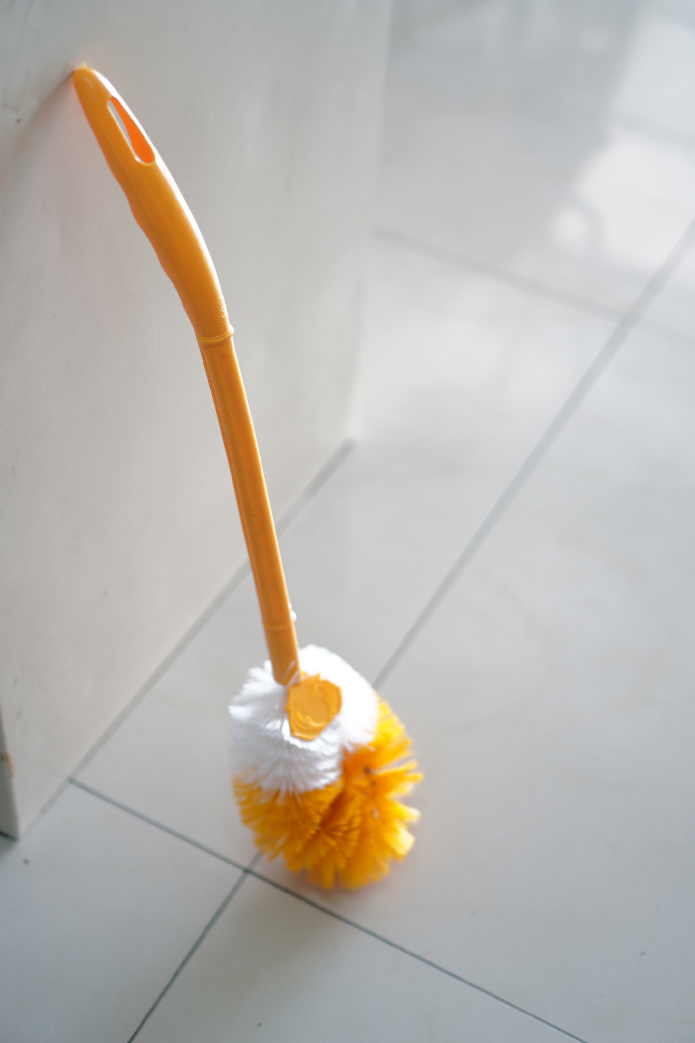 Yellow-handled brush with white and yellow bristles leaning against a wall on a tiled floor