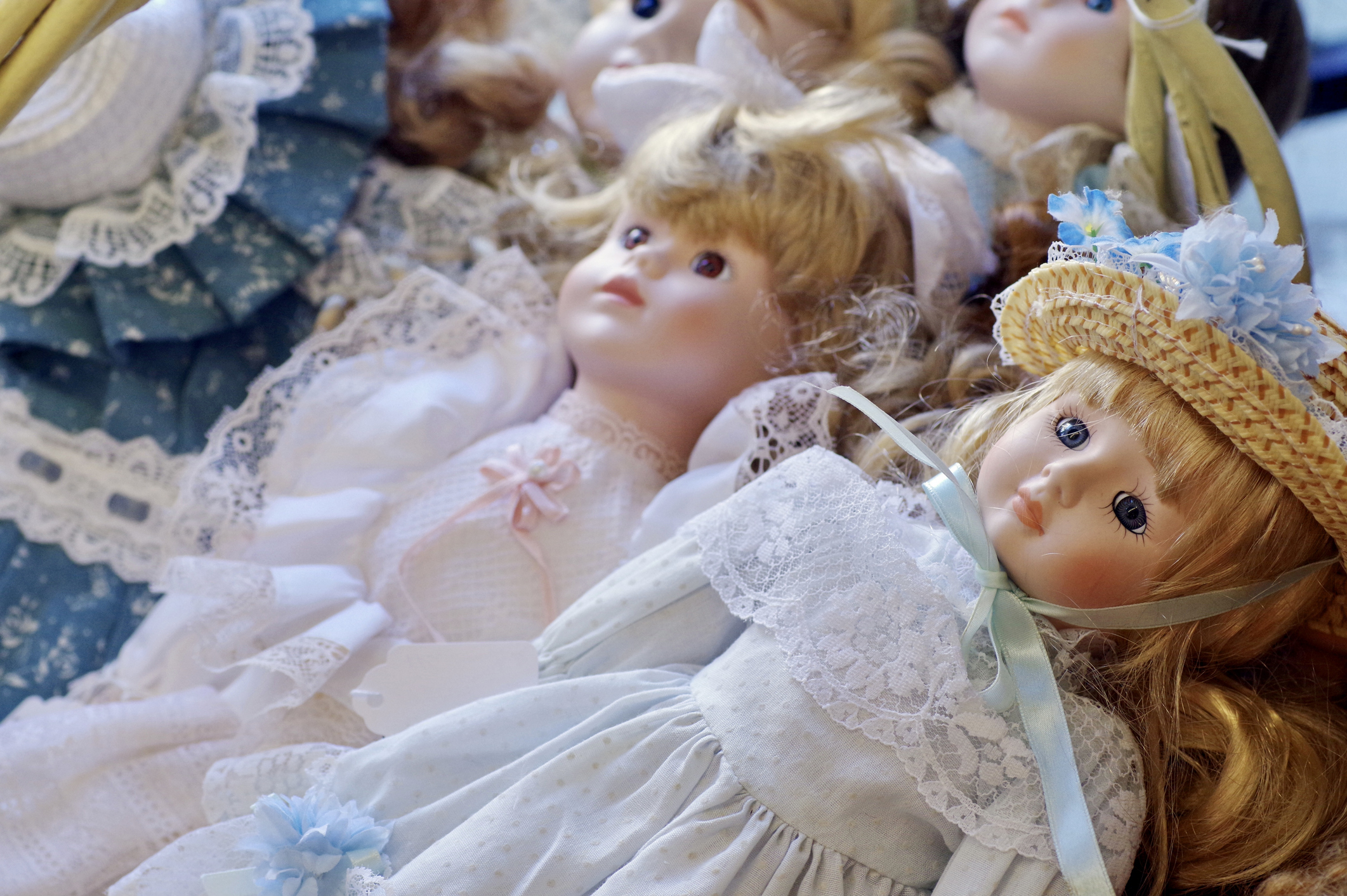 Multiple porcelain dolls with intricate dresses and hats are arranged close together
