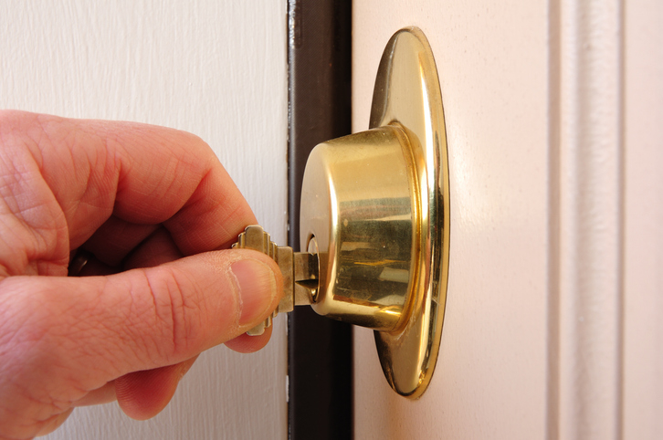 A close-up of a hand turning a key in a brass deadbolt lock on a wooden door