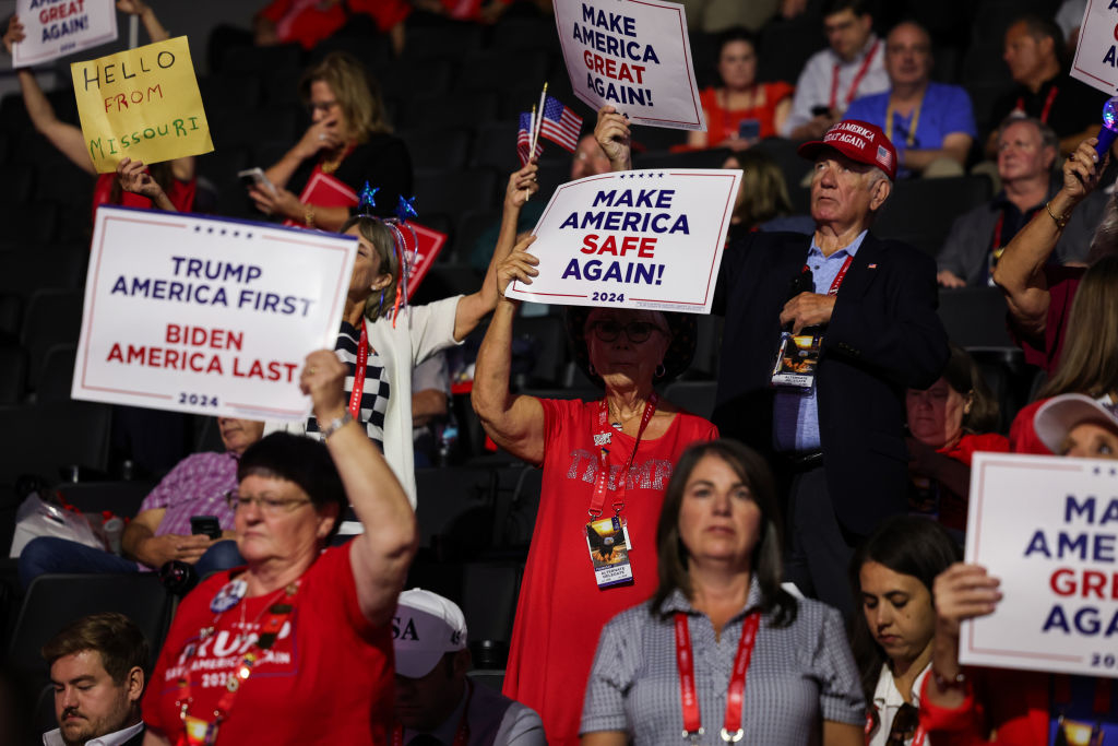 People at a rally hold signs with messages like &quot;Make America Great Again,&quot; &quot;Make America Safe Again,&quot; and &quot;Hello from Missouri!&quot; Some wear MAGA hats