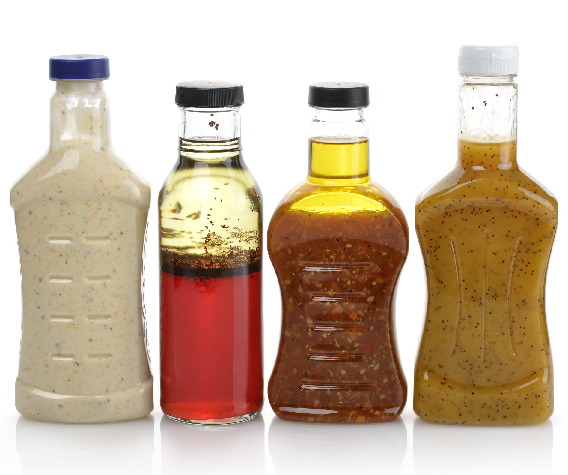 Four bottles of various salad dressings are lined up. From left to right: creamy dressing, vinegar-based dressing, a spicy dressing, and a mustard-based dressing
