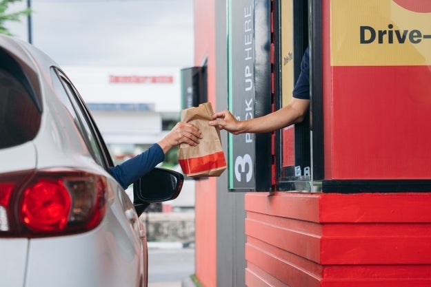 A person in a car receives a paper bag of food from a fast-food drive-thru window