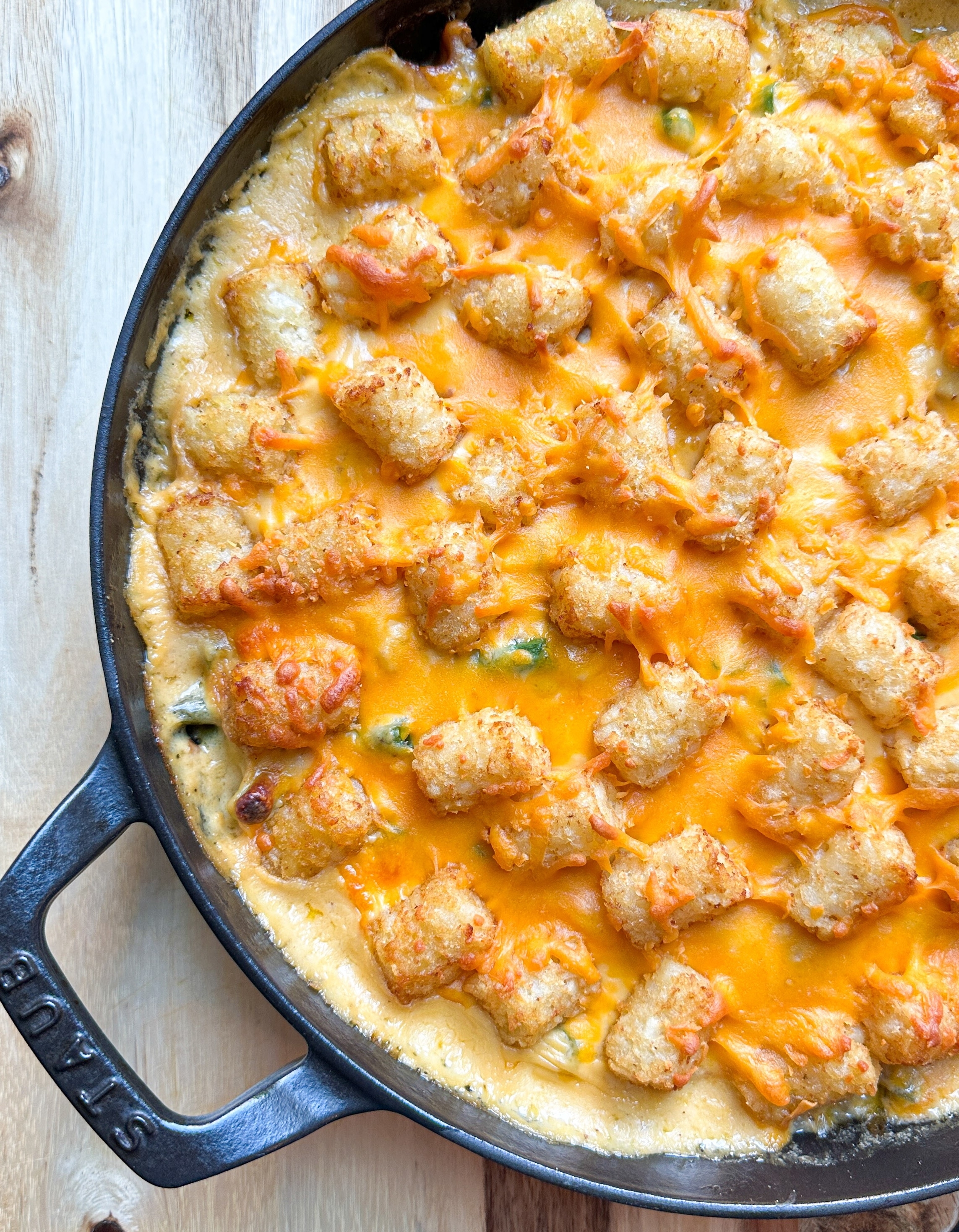 Close-up of a skillet containing a cheesy tater tot casserole with vegetables and ground meat