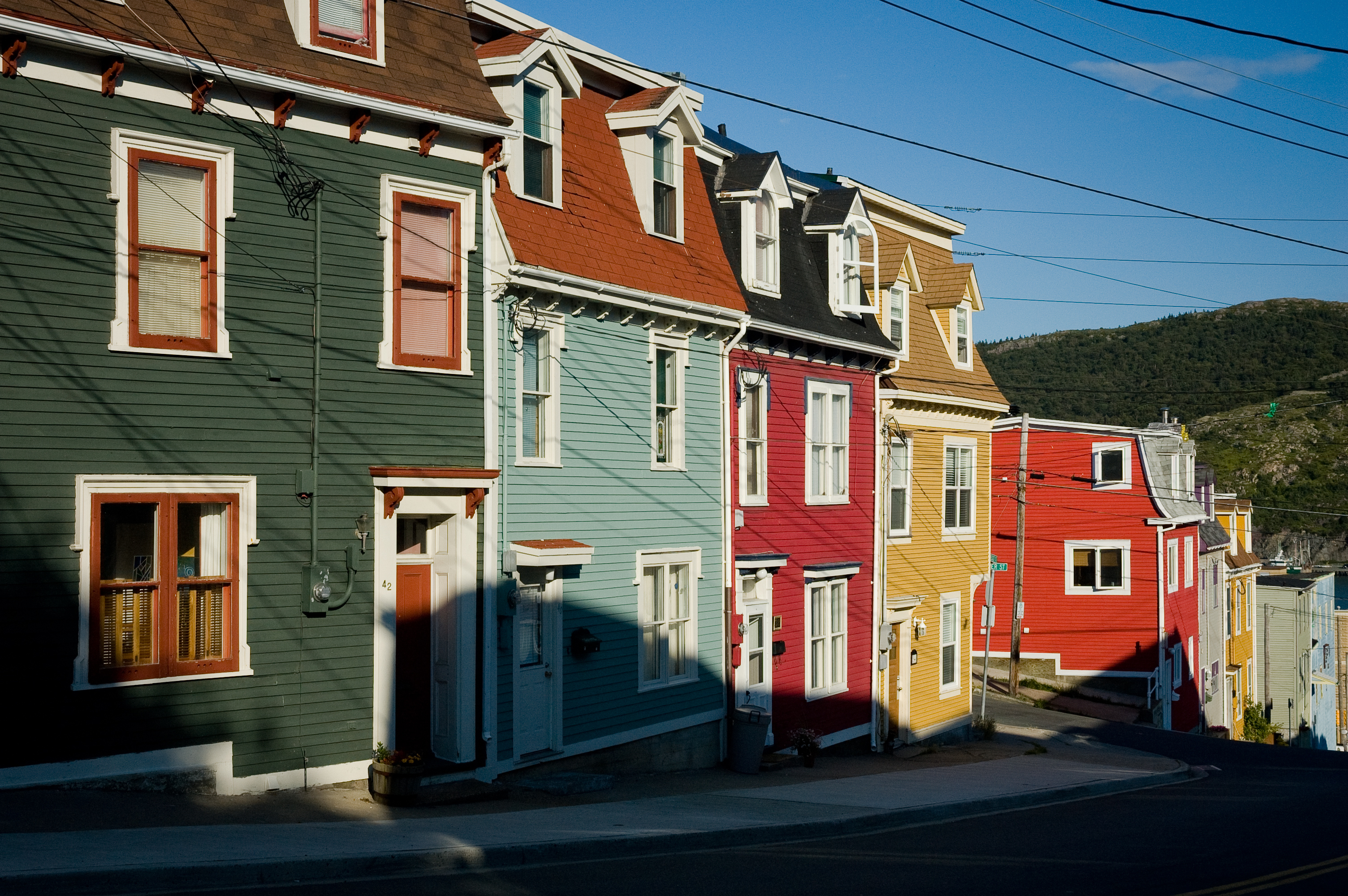 Row of colorful houses on a steep street with a hill in the background, displaying architectural diversity and charm