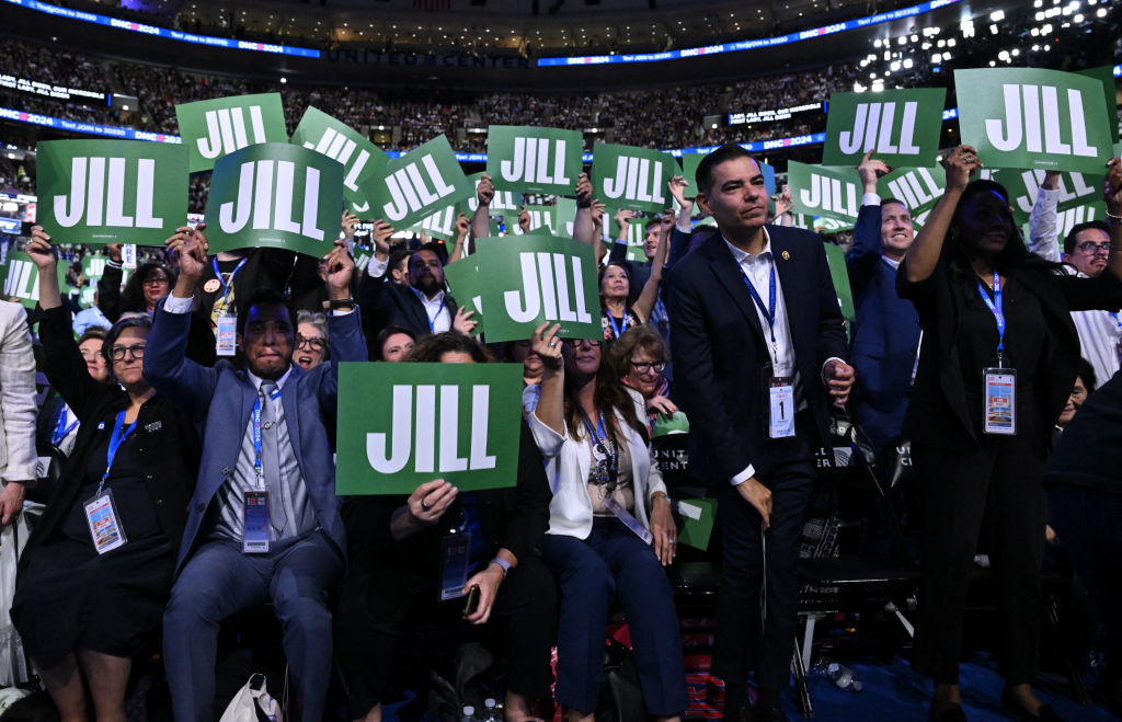 A large crowd holds up green signs that read &quot;Jill&quot; at a rally. Several people are wearing badges and lanyards, indicating the event is likely political