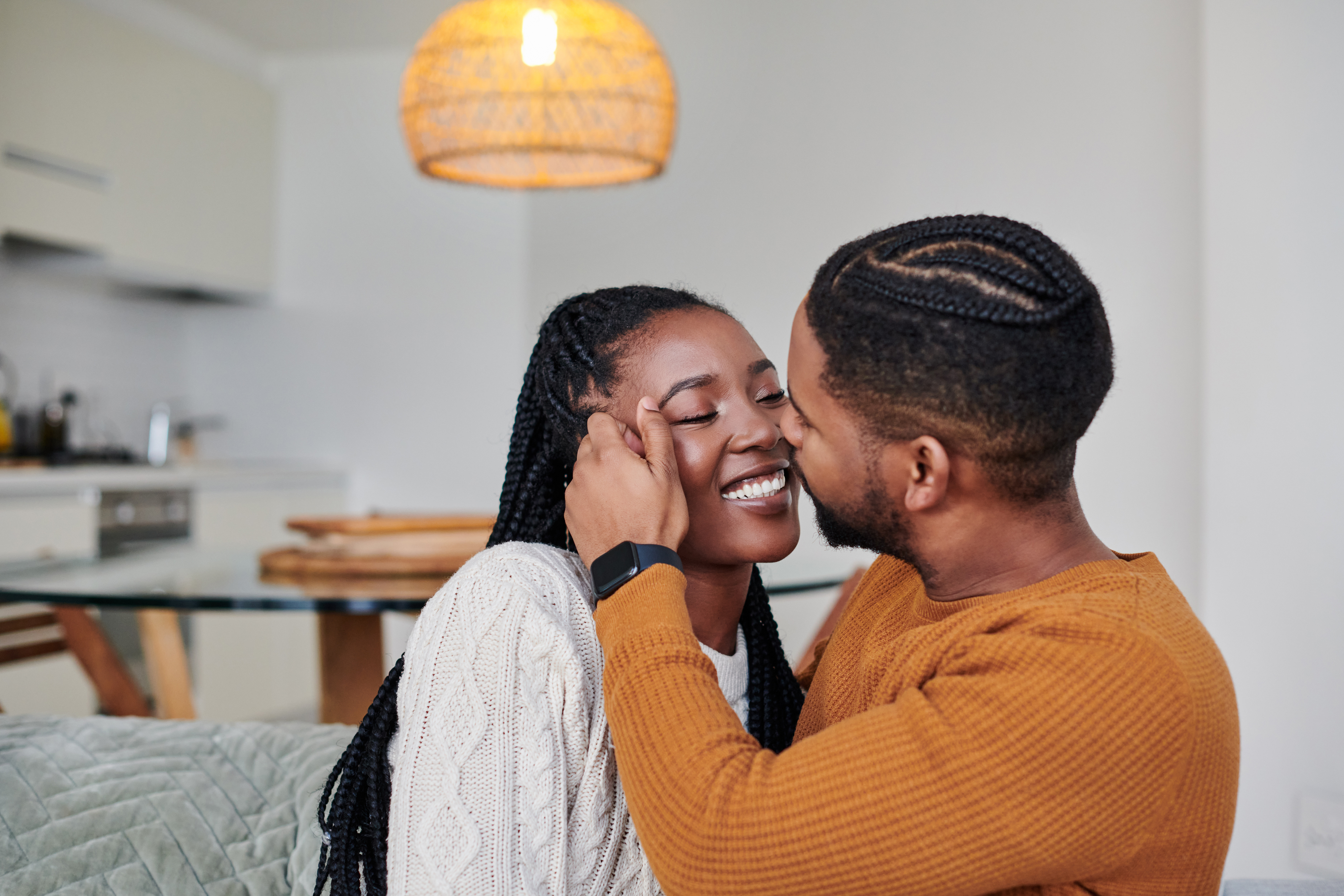 Two people sitting in a cozy room, smiling and sharing a tender moment as they lean into each other affectionately