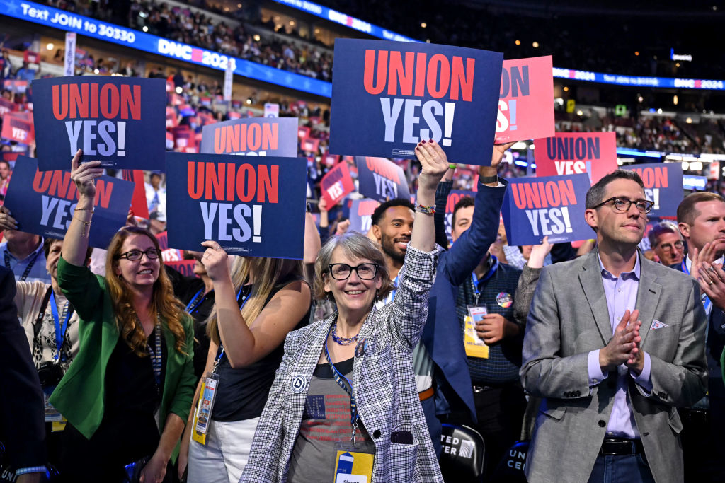 A group of people at a lively indoor event hold up &quot;Union Yes!&quot; signs. They appear enthusiastic and supportive