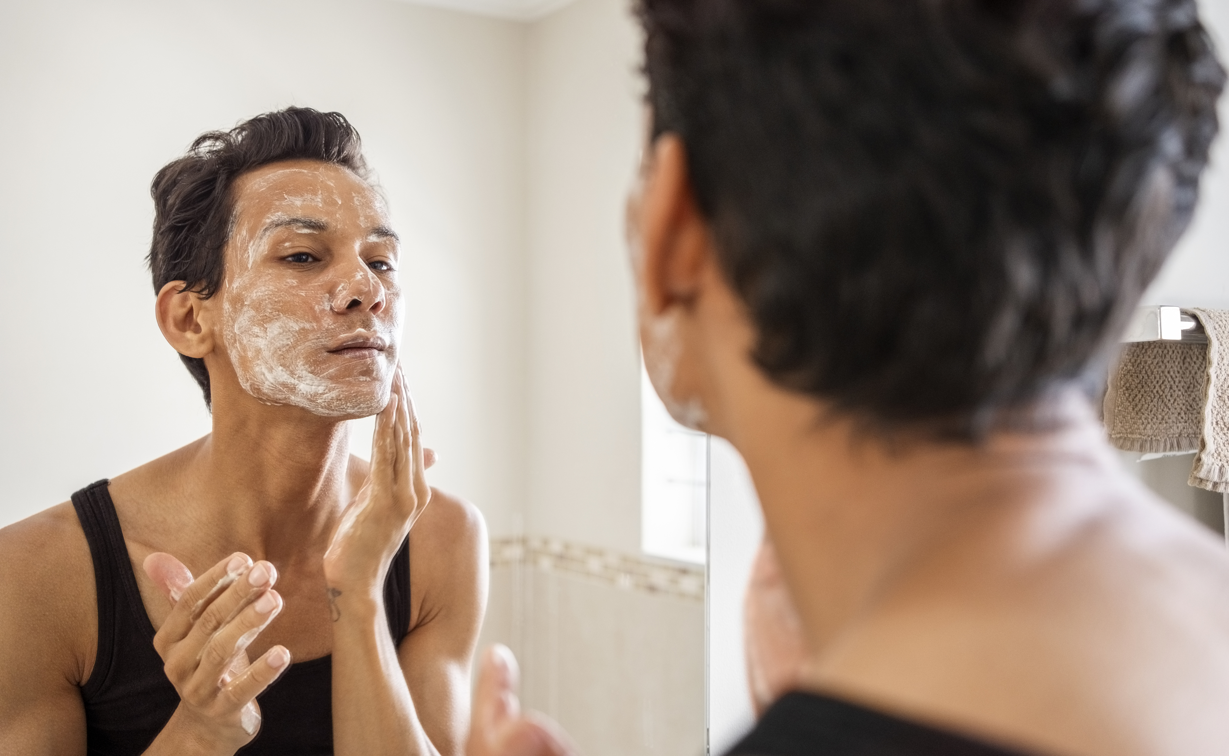 Person applying a face mask in a bathroom while looking in a mirror