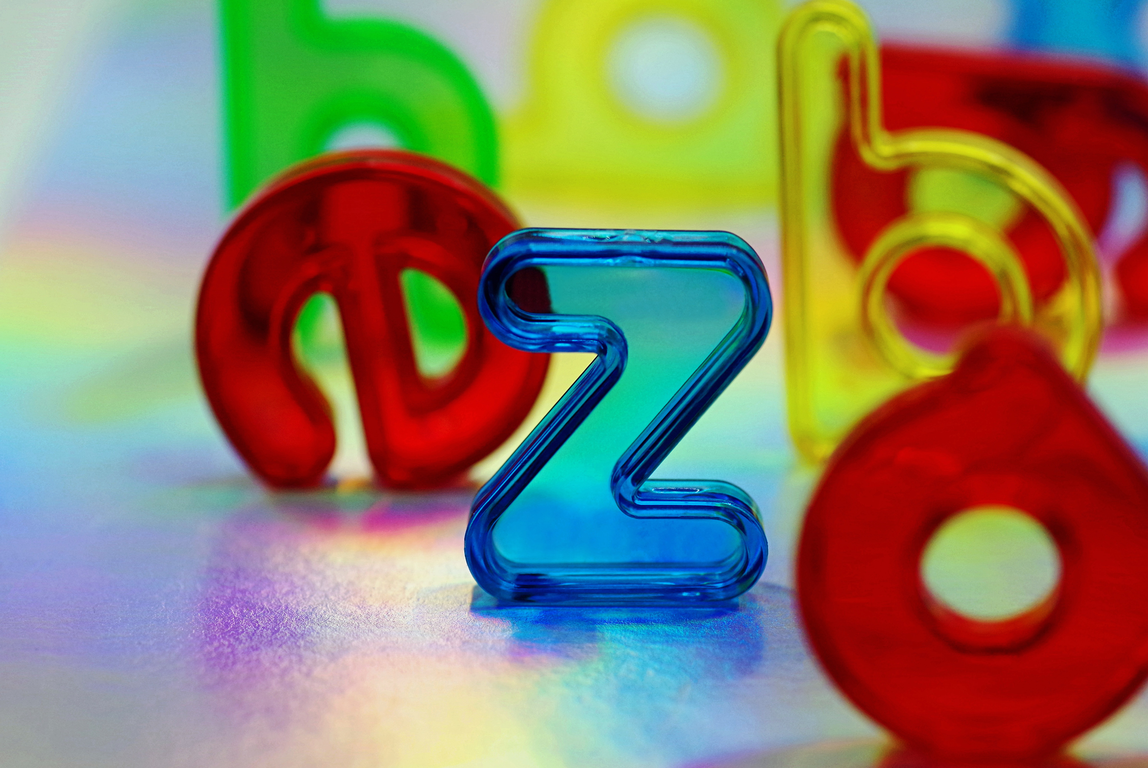 Colorful, transparent plastic letters, including 'z,' 'a,' 'b,' and 'd,' are arranged on a reflective surface