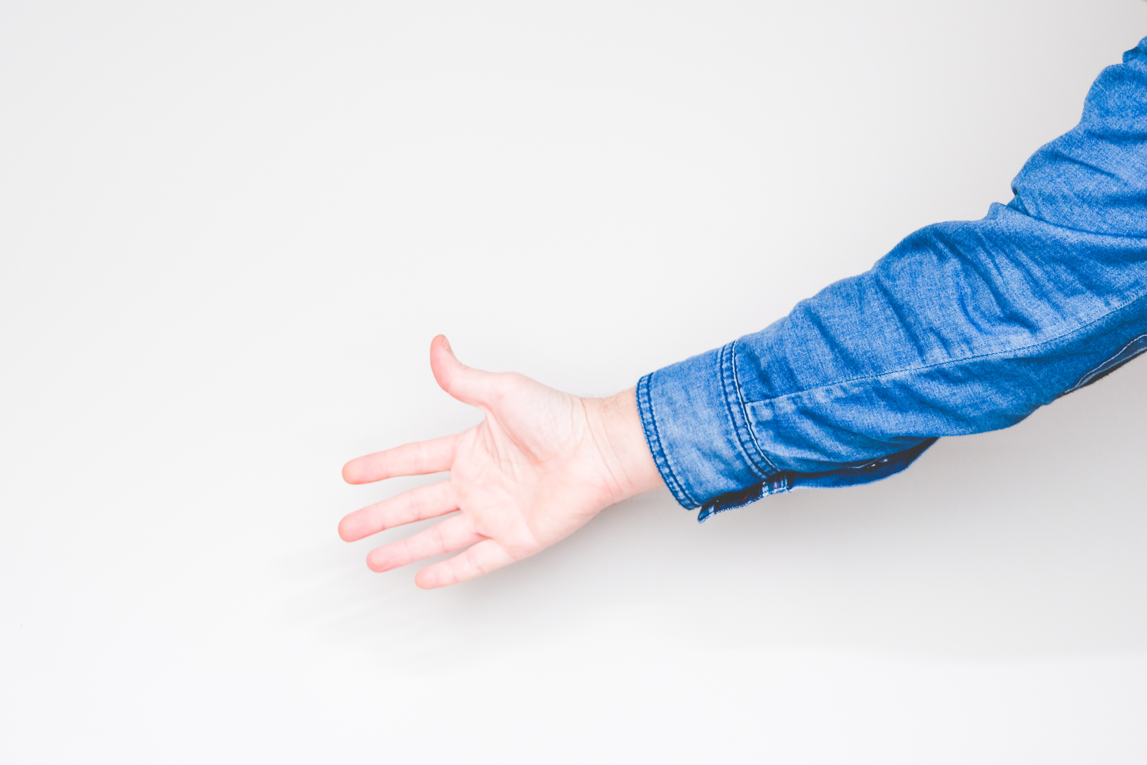 A person extends their hand for a handshake. The person is wearing a denim jacket