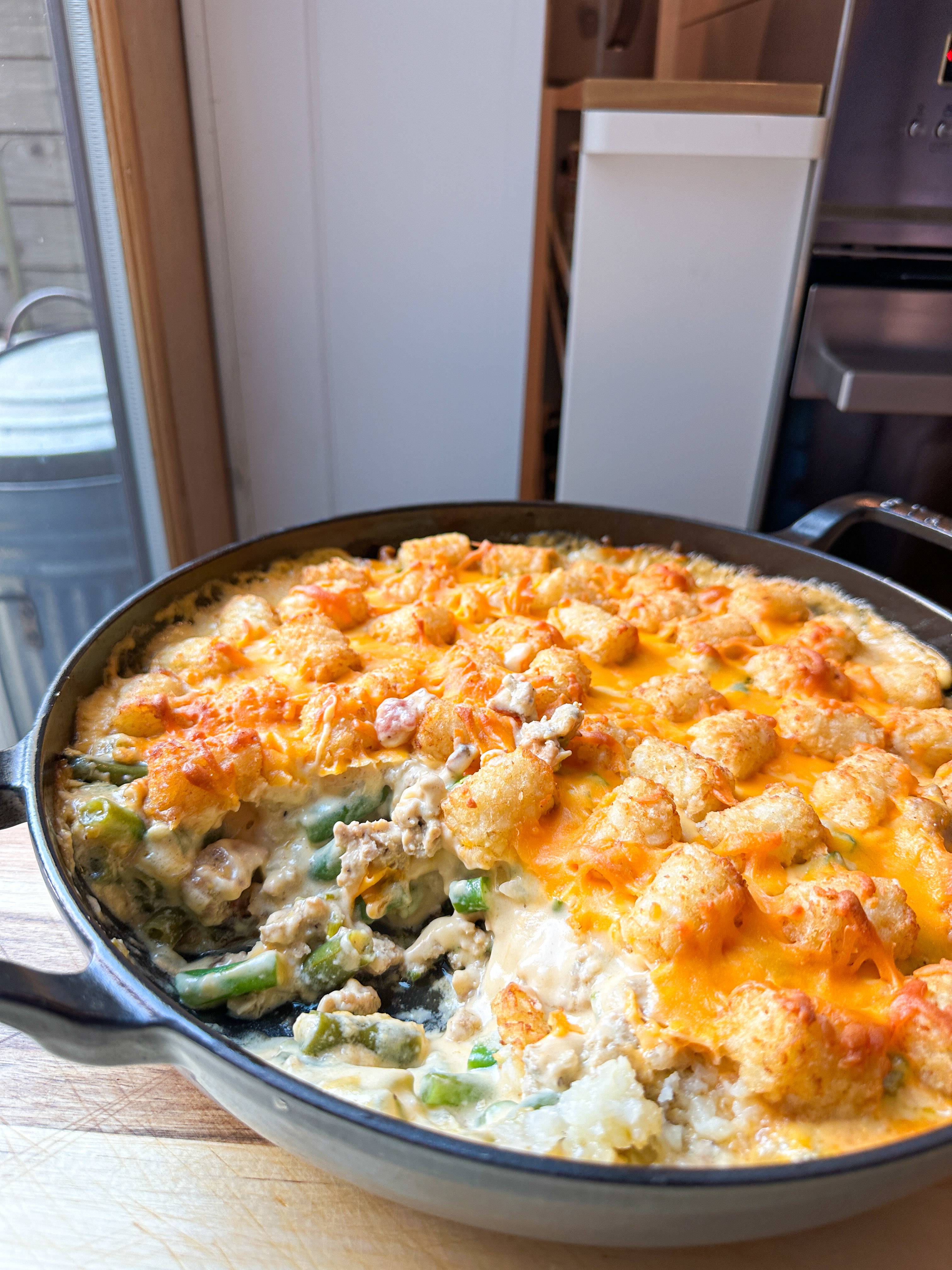 A closeup of a hotdish with mixed vegetables and melted cheese, partially served, sitting on a kitchen countertop