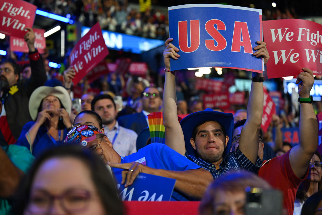 A crowd holds signs reading &quot;USA&quot; and &quot;We Fight. We Win.&quot; at a large indoor event, possibly a rally or convention