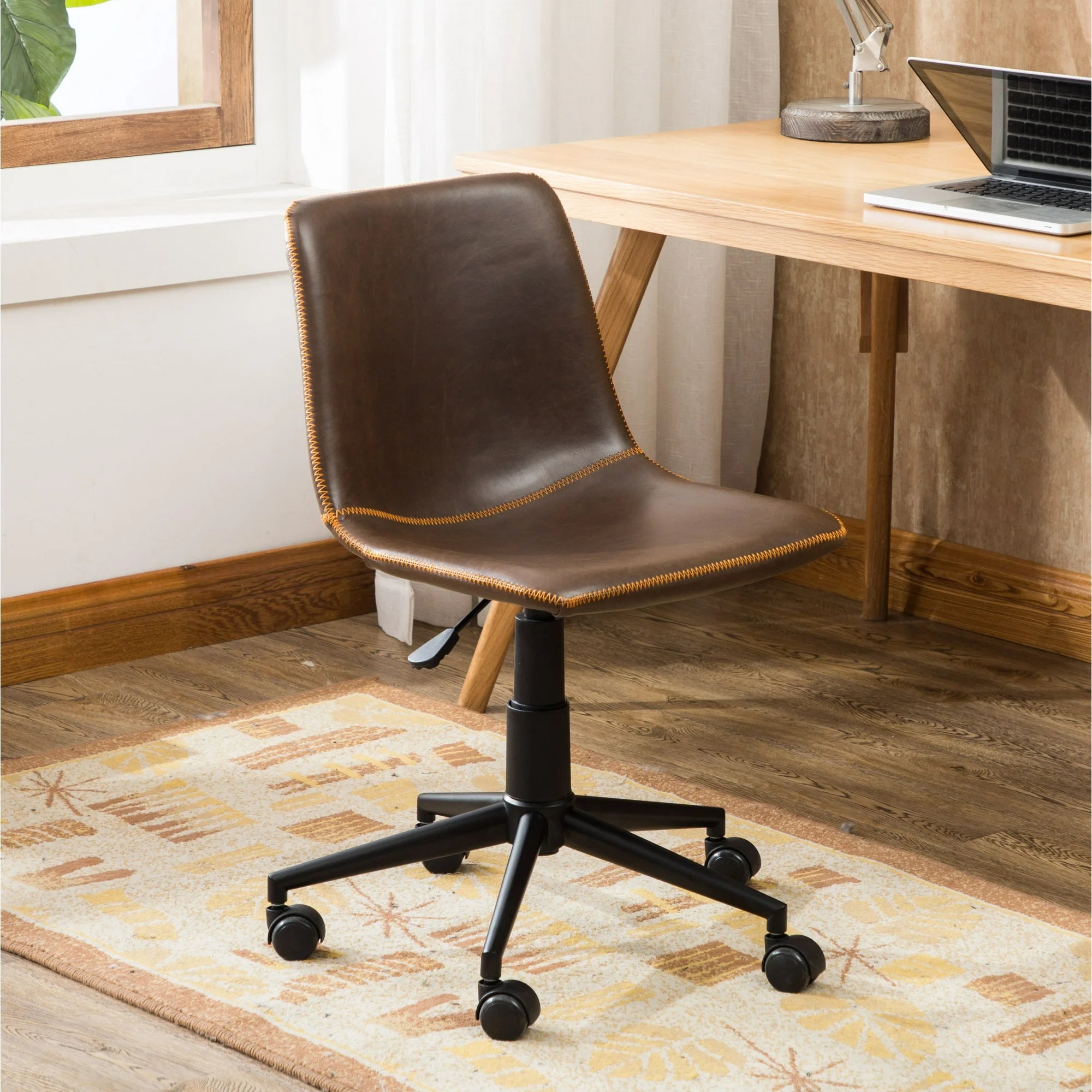 Kursi kantor kulit coklat antik dengan tinggi dan roda yang dapat disesuaikan, ditempatkan di sebelah meja kayu dengan laptop dan buku -buku di atasnya, dalam pengaturan kantor rumah