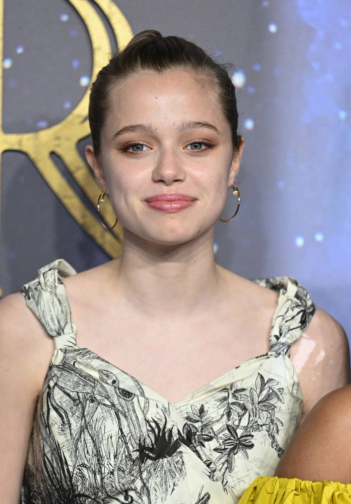 Shiloh Jolie-Pitt smiles while wearing a floral-patterned dress on the red carpet
