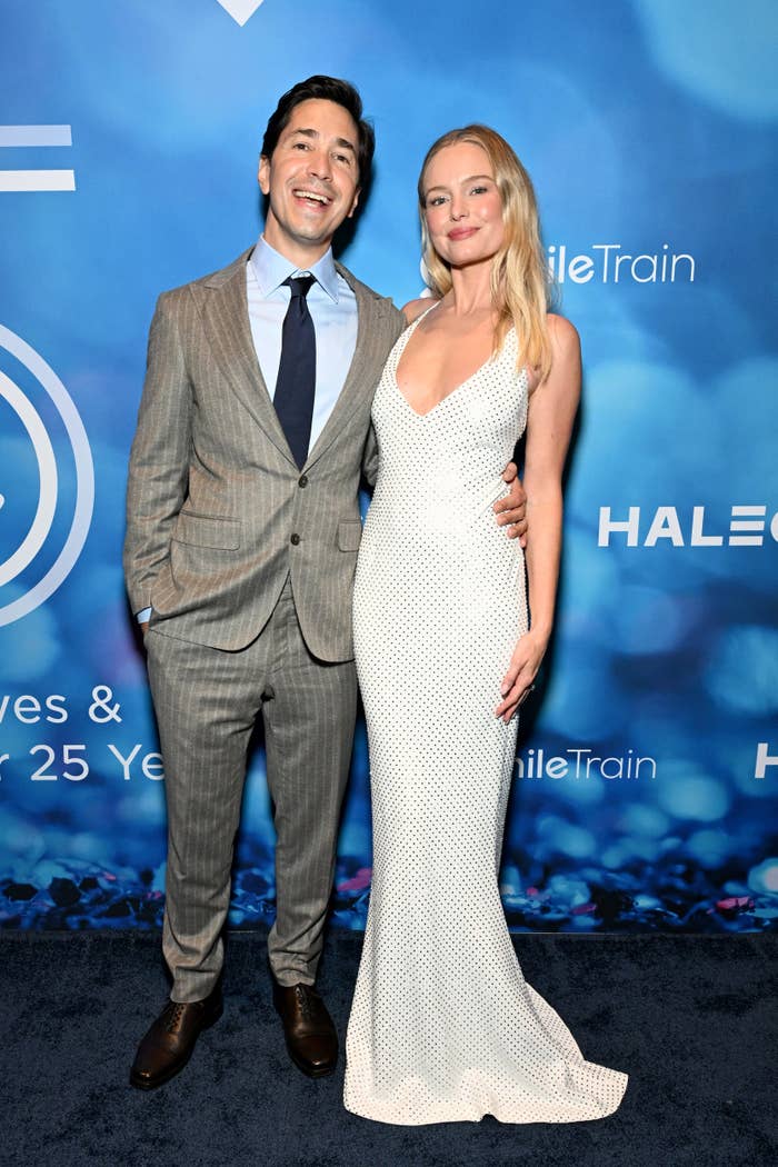 Justin Long in a gray suit and Kate Bosworth in a white gown pose together at a red carpet event