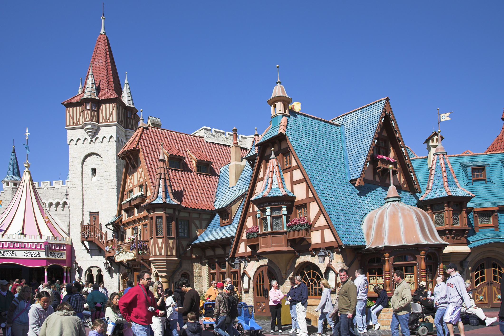 Crowded theme park with people walking in front of colorful, fairy-tale-like buildings. No specific text or celebrities included
