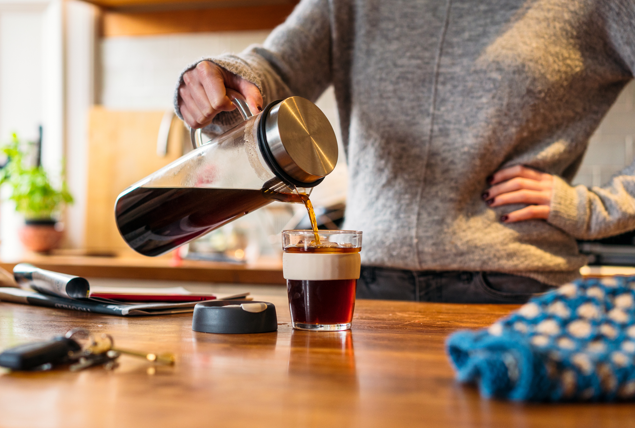 Person pouring coffee from a french press into a glass on a kitchen counter
