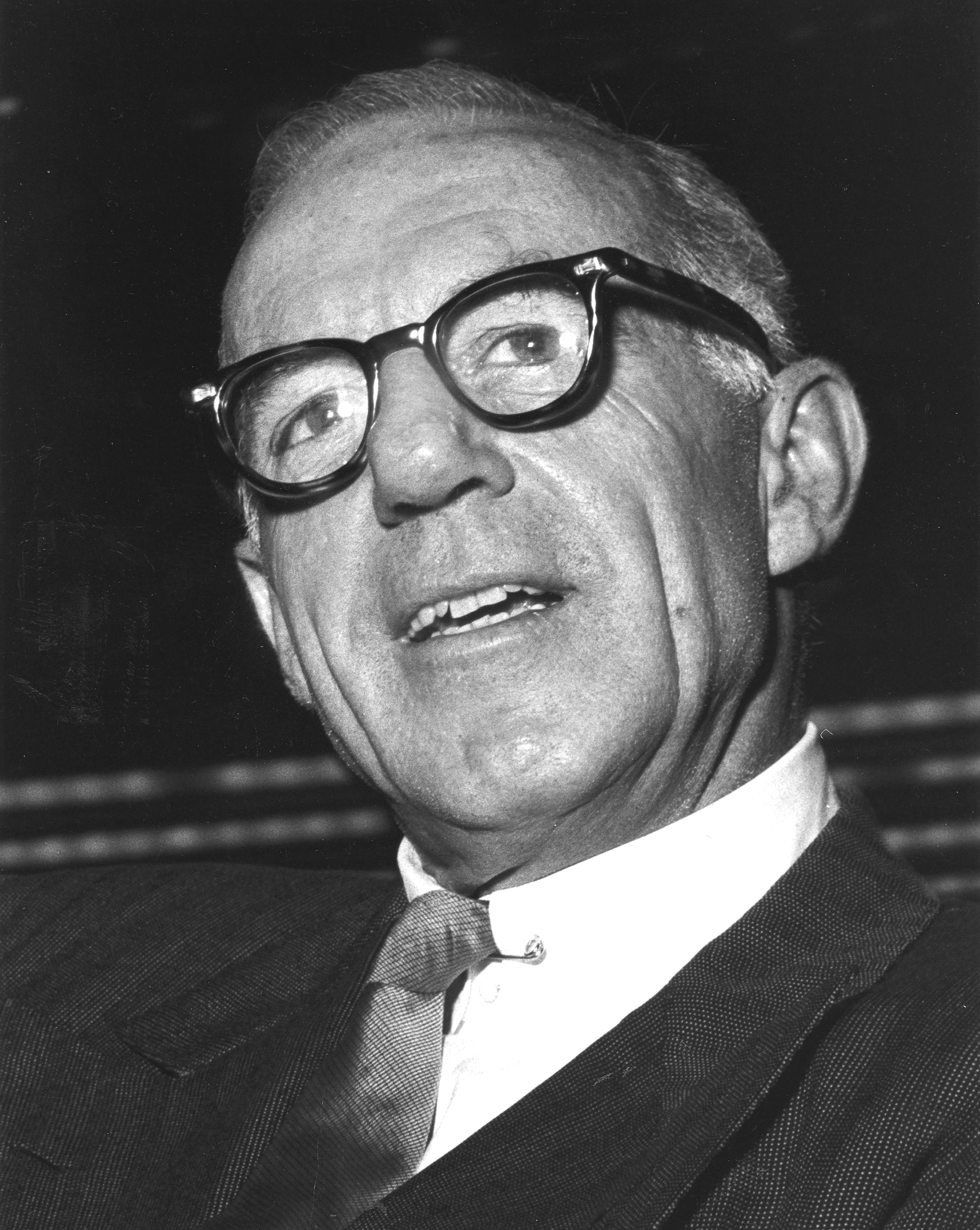 Dr. Benjamin Spock  in glasses and a suit smiles, looking upwards