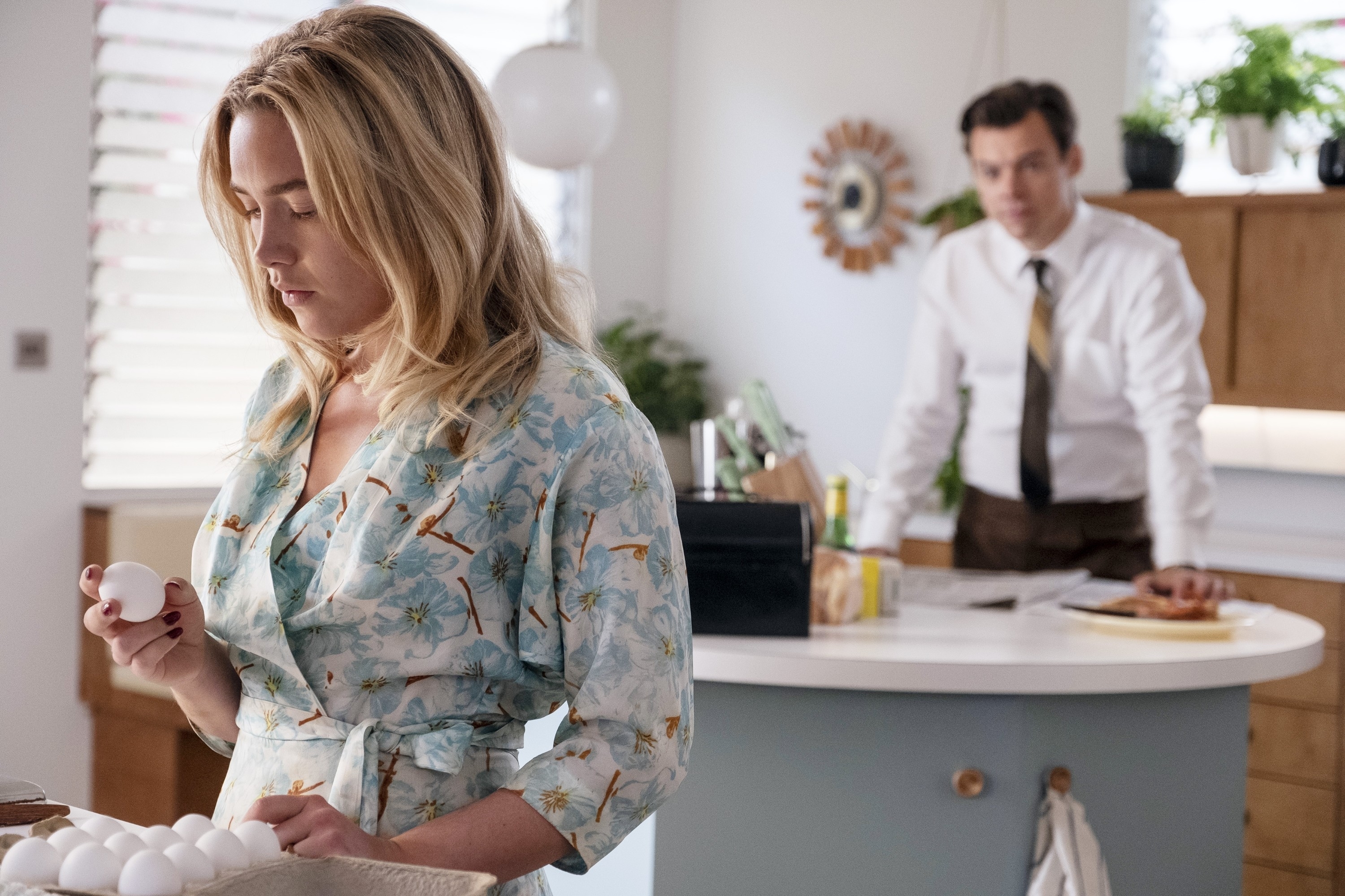Florence Pugh holding an egg while Harry Styles stands behind her in the kitchen in Don't Worry Darling"
