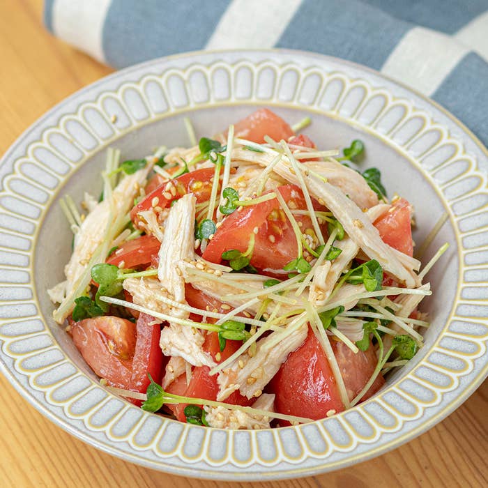 美味しそうなサラダが盛り付けられた白い皿。サラダチキン、トマト、貝割れ大根が混ざっている。