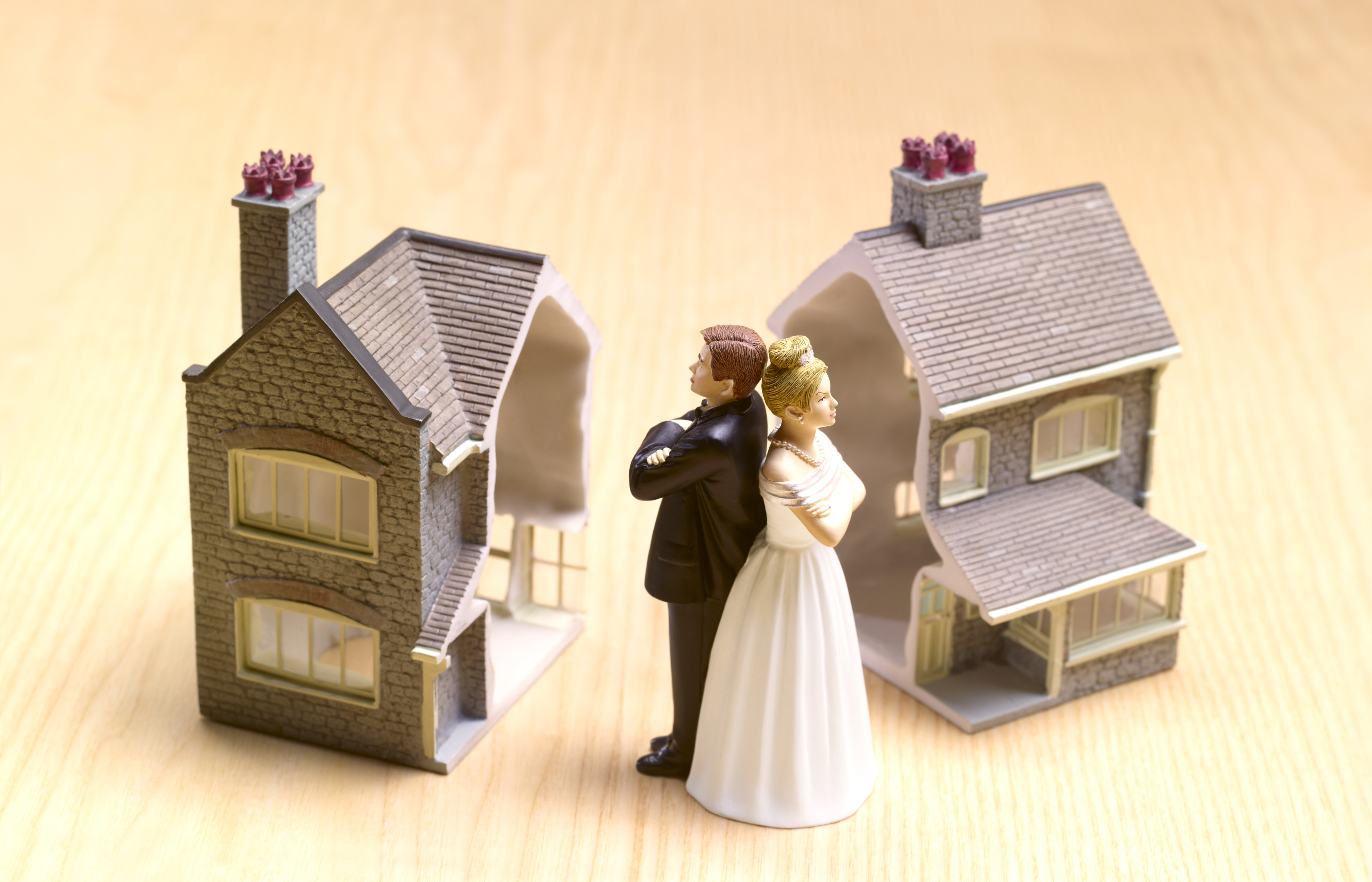 Bride and groom figurines stand back to back, each next to a split house representing divorce or separation
