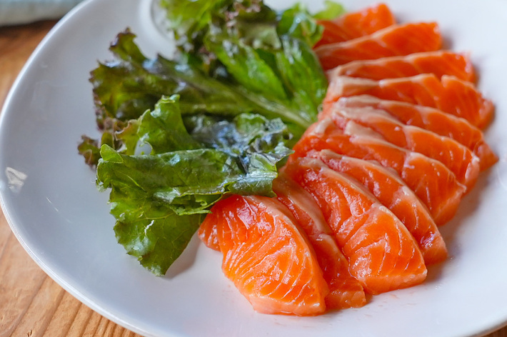 生鮭の刺身と緑の葉物野菜が白い皿に盛り付けられています。