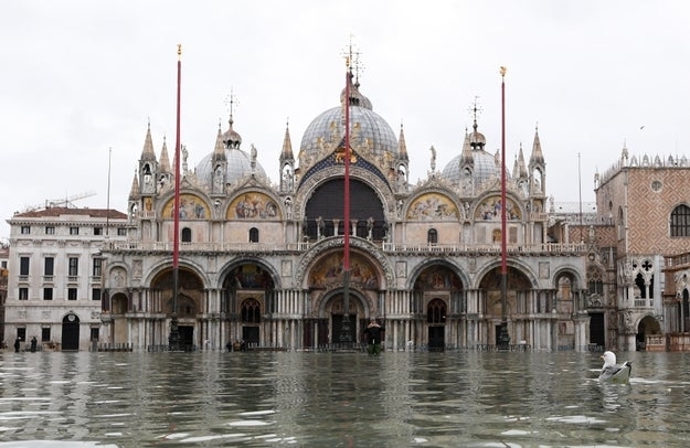 St. Mark's Basilica in Venice is shown partially submerged due to flooding, with water covering parts of the square in front of the cathedral