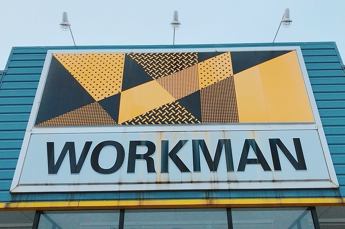 Storefront with a large &ldquo;WORKMAN&rdquo; sign featuring geometric patterns above it, flanked by light fixtures on top