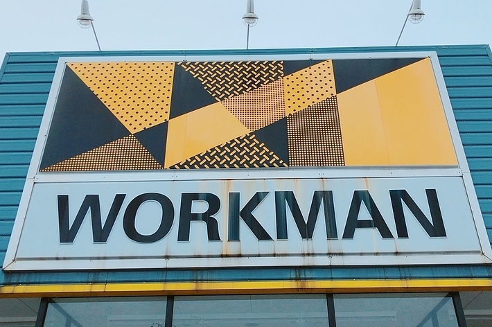 The image shows a building with a geometric yellow and black sign that reads &ldquo;WORKMAN.&quot;