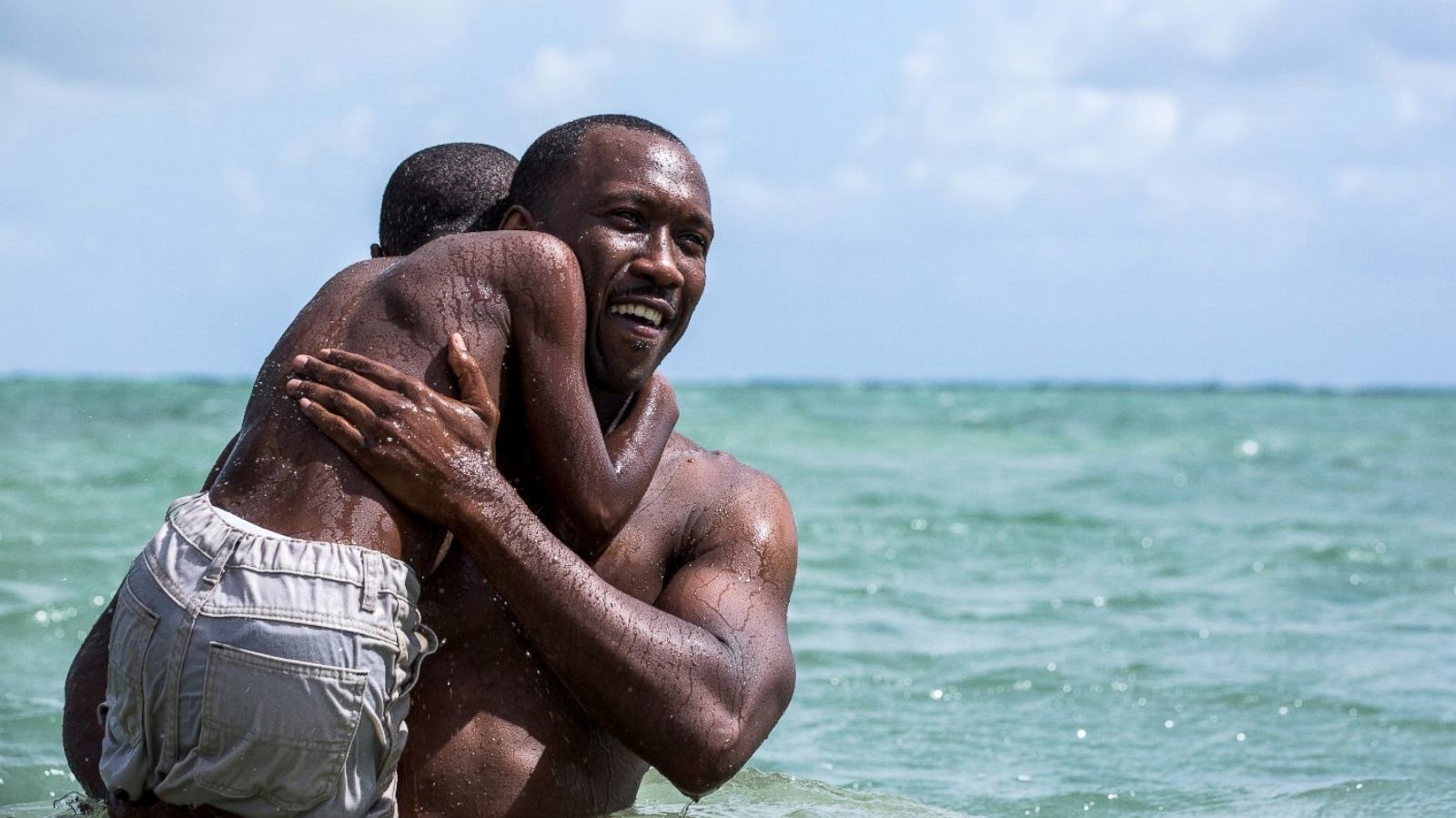 Man and child embrace in the ocean with smiles, enjoying the water and each other's company