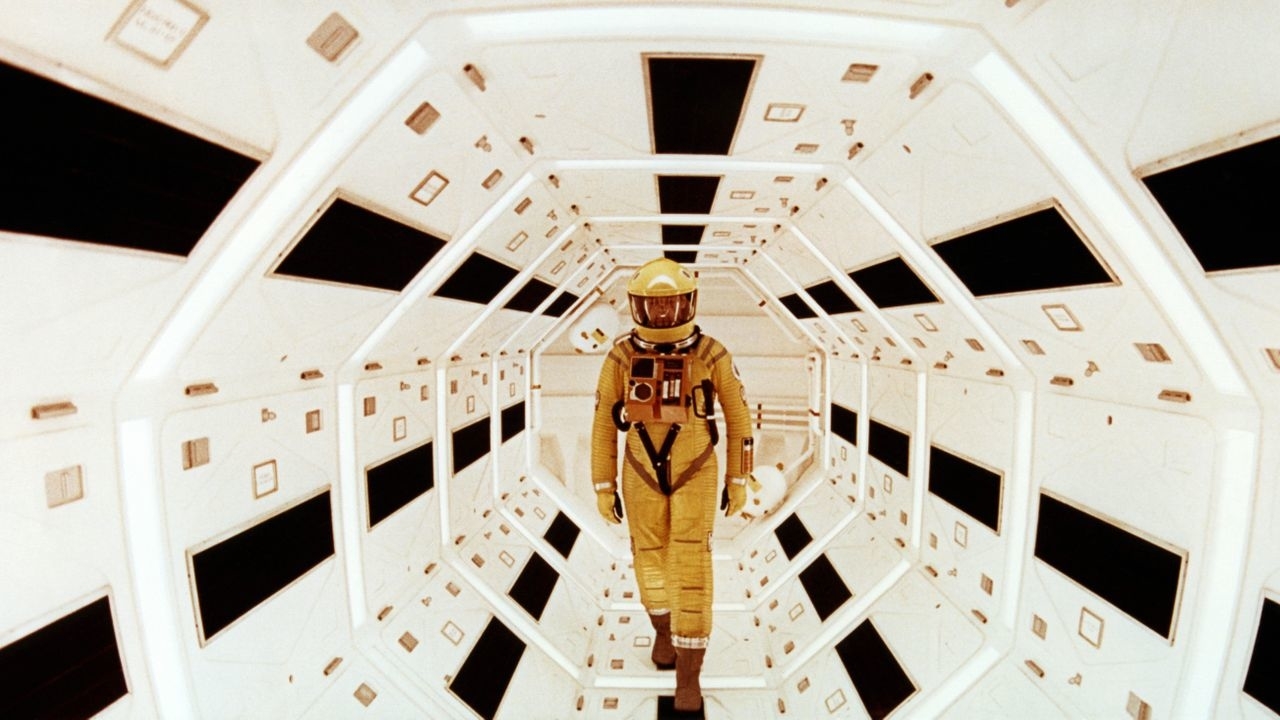 An astronaut in a spacesuit walks through a futuristic, hexagonal passage with geometric patterns from "2001: A Space Odyssey."