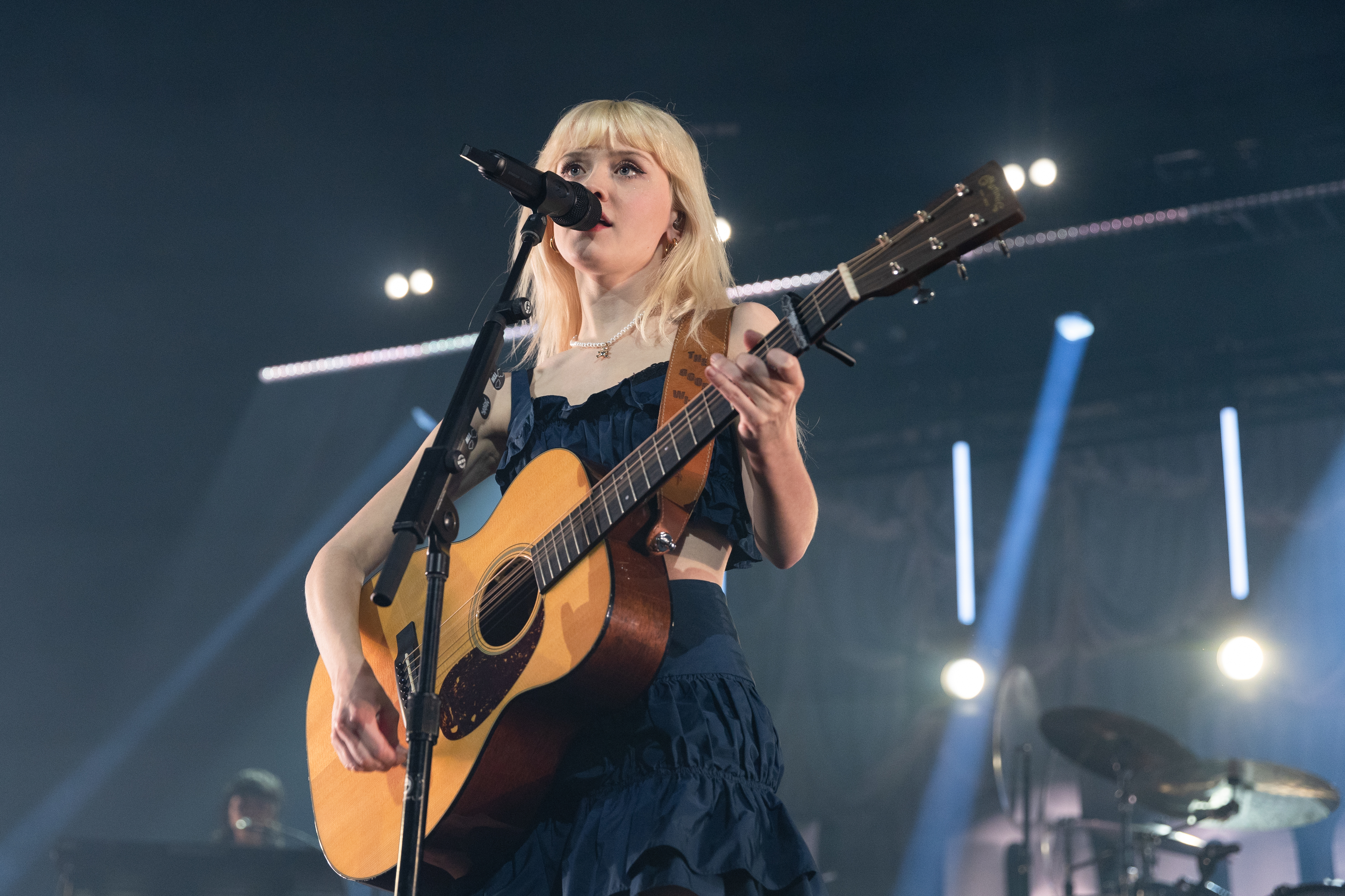 Maisie Peters sings and plays an acoustic guitar on stage during a live concert