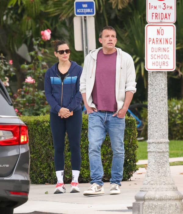 Ben Affleck and Jennifer Garner on a sidewalk near a &quot;No Parking During School Hours&quot; sign. Both are dressed casually; Affleck in jeans and a hoodie, Garner in workout attire