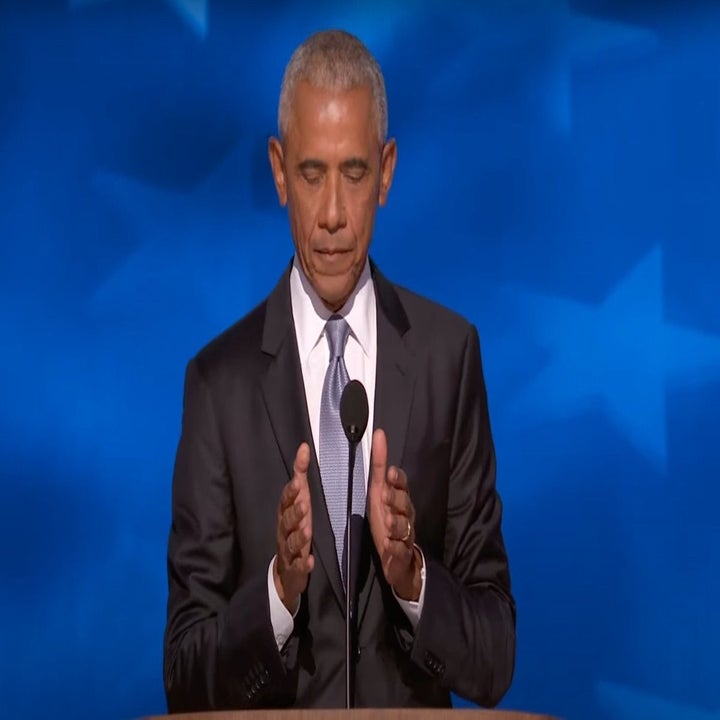 Barack Obama stands at a podium, wearing a suit and tie, with eyes closed and hands raised near the microphone. Blue background with stars