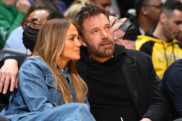 Jennifer Lopez and Ben Affleck sit closely together at an event, with Ben&#x27;s arm around Jennifer. Both are wearing casual clothing